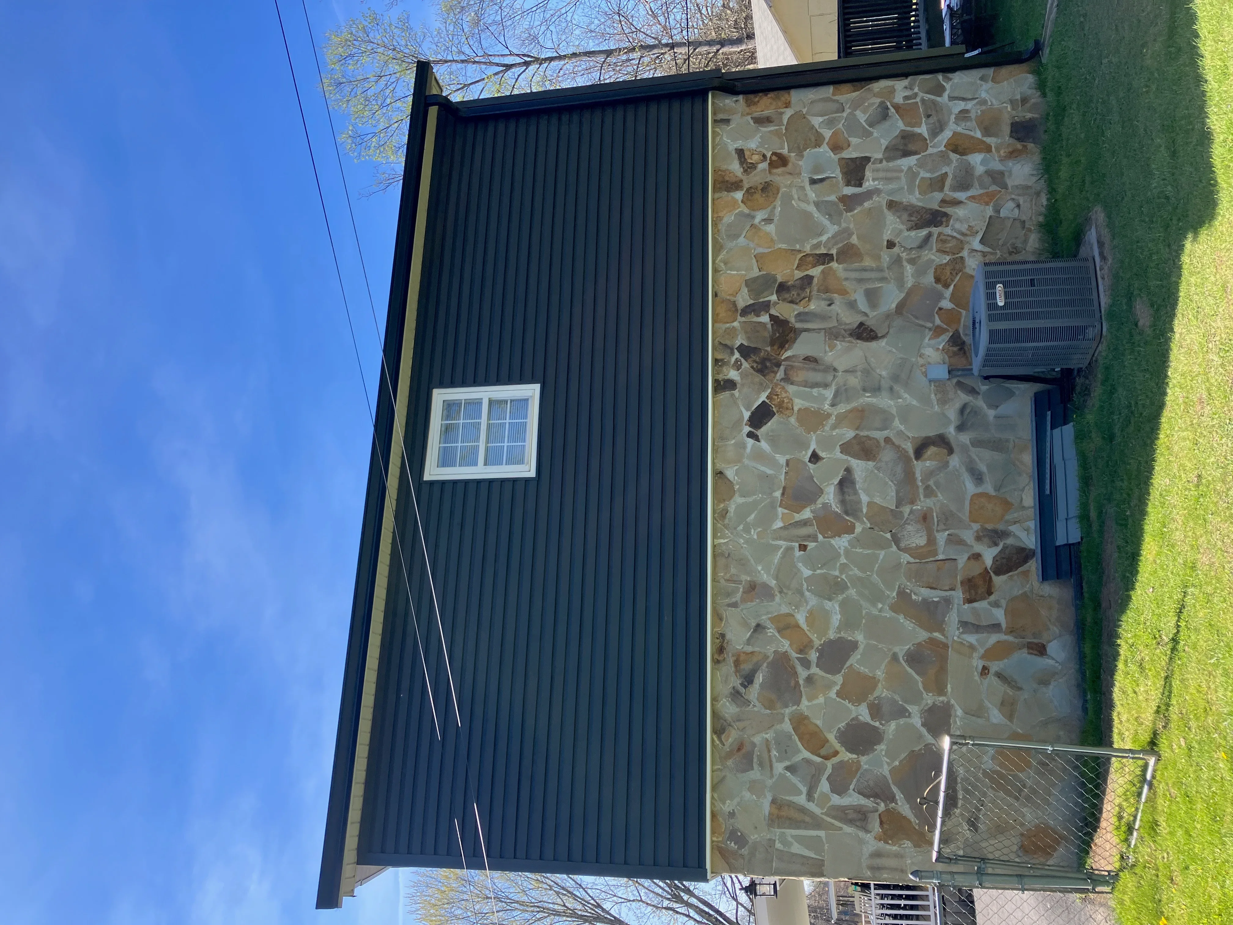Corrugated metal and stone veneer exterior with installed gutters and downspout system