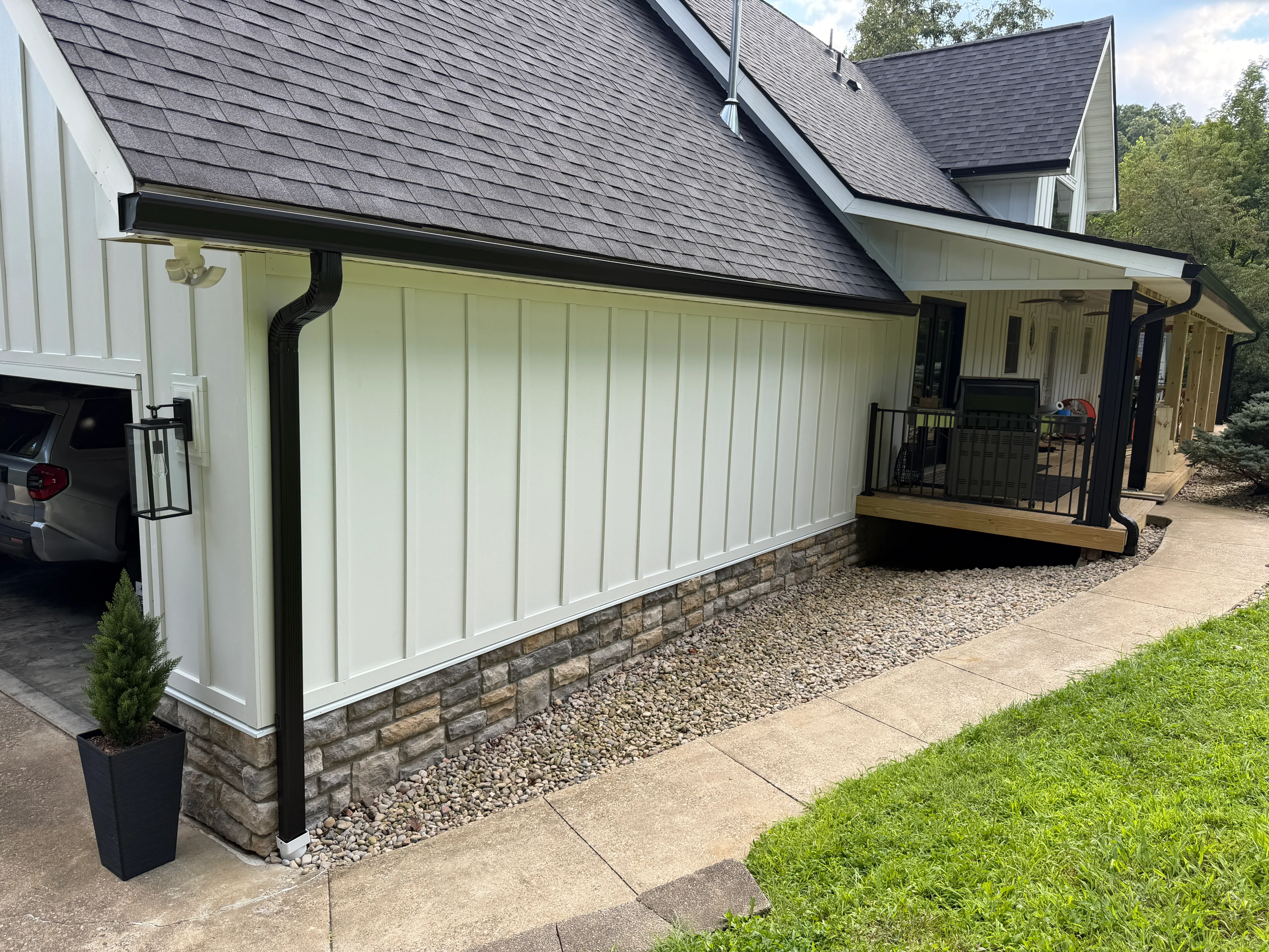 Black aluminum gutters and downspouts on white siding with stone veneer base and gravel drainage