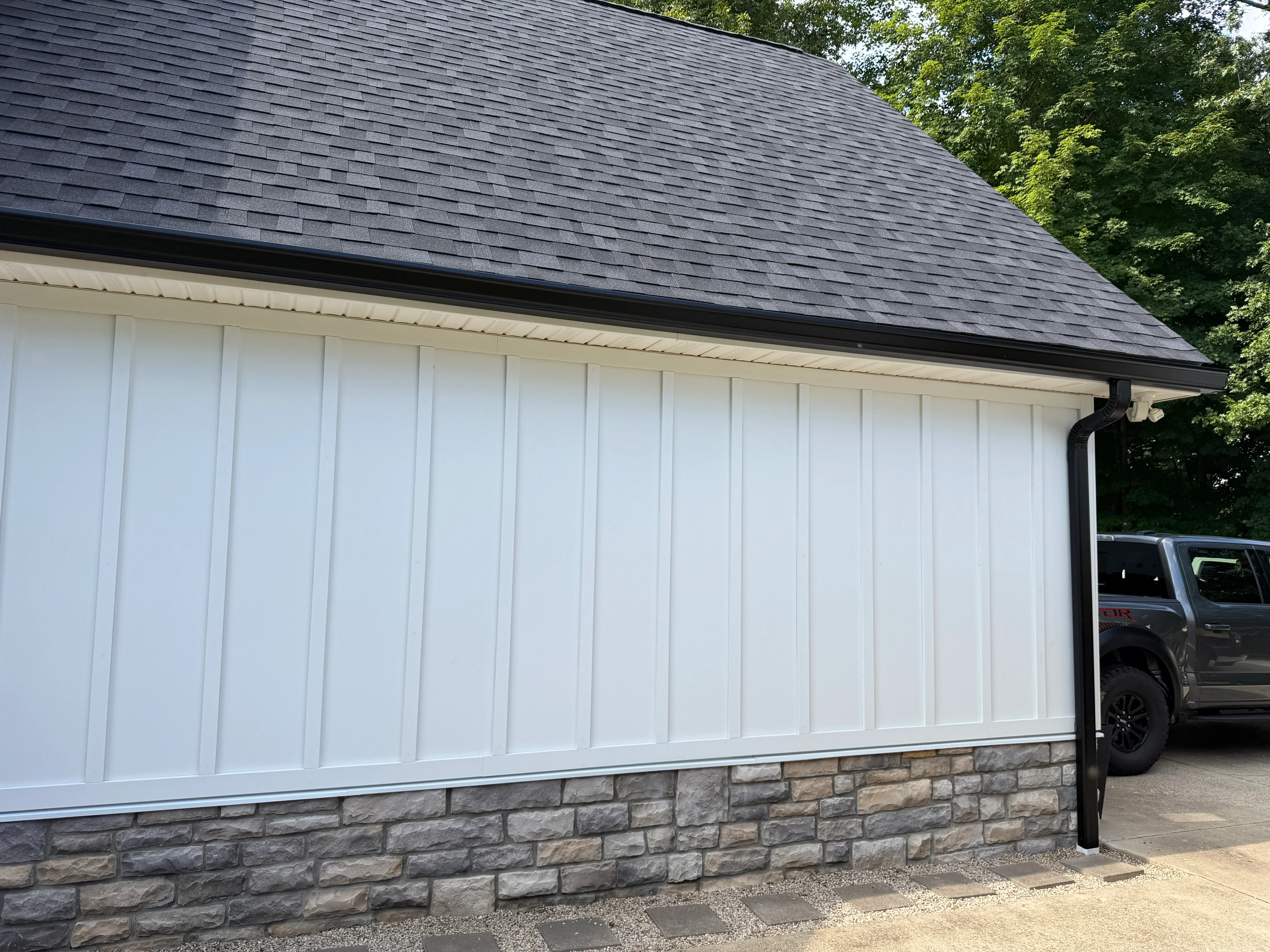 Black aluminum gutters and downspout on white-sided garage with dark roof shingles