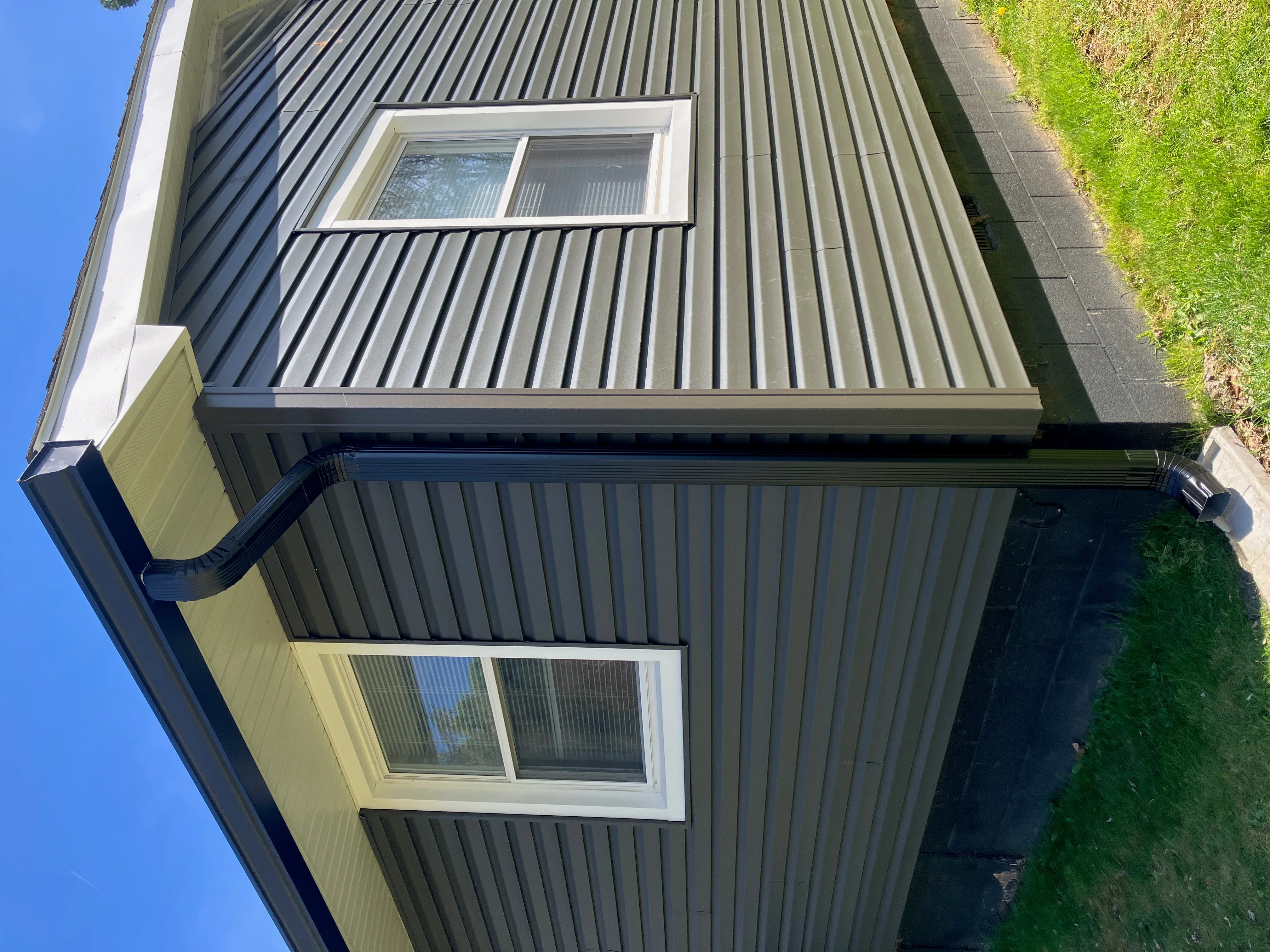 Metal gutter system with white trim and black downspout on corrugated metal siding
