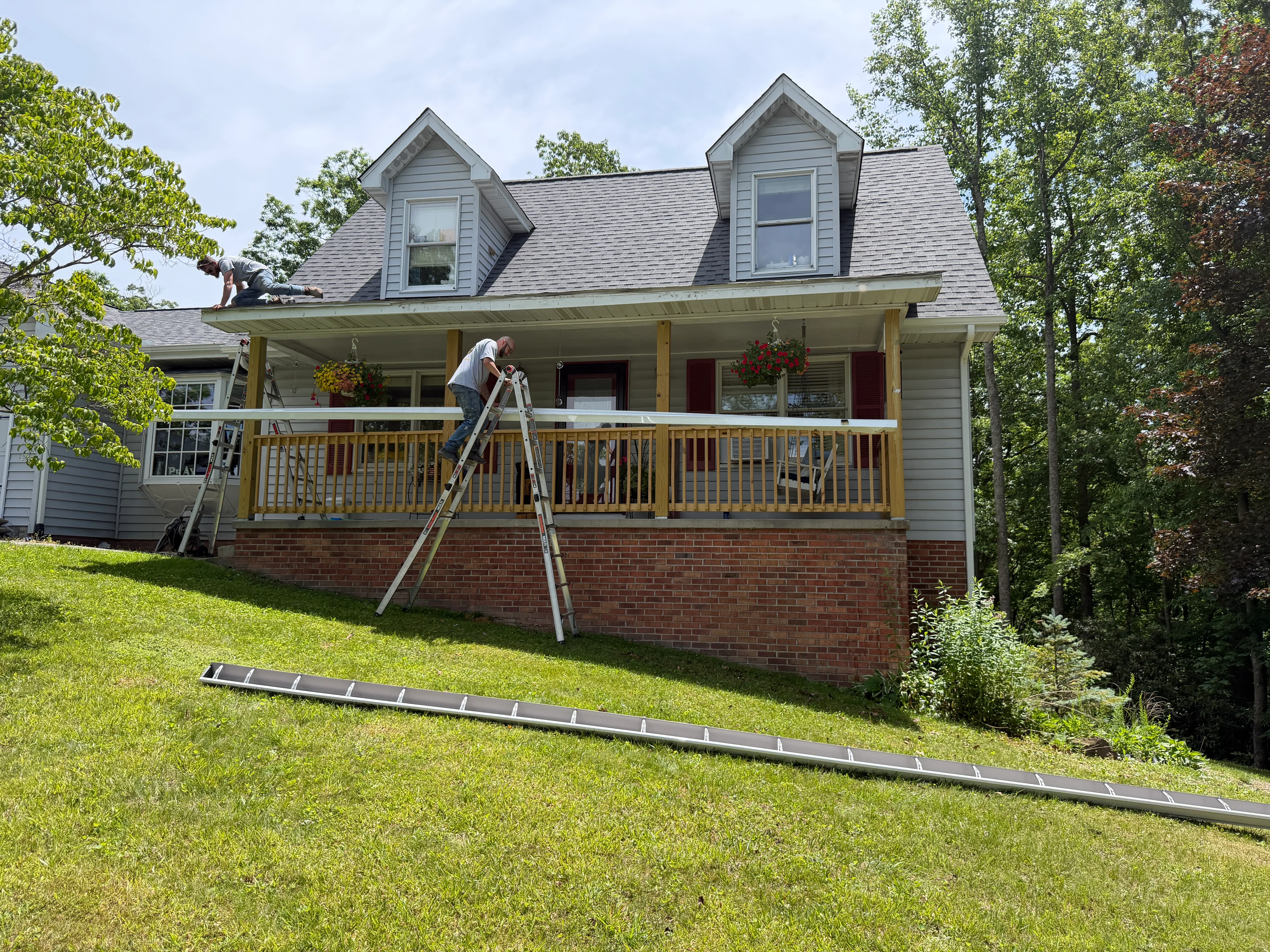 Gutter installation on two-story home with brick base and wood siding, worker on ladder