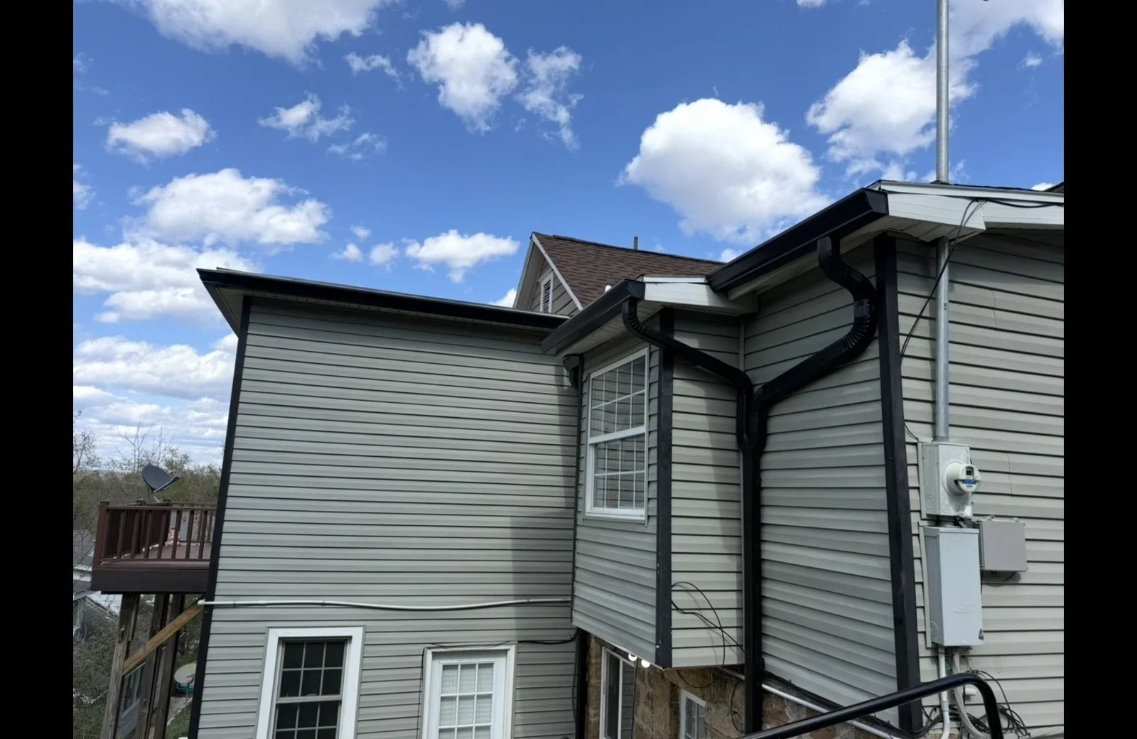Gray seamless gutters with black fascia and downspout installation on residential home