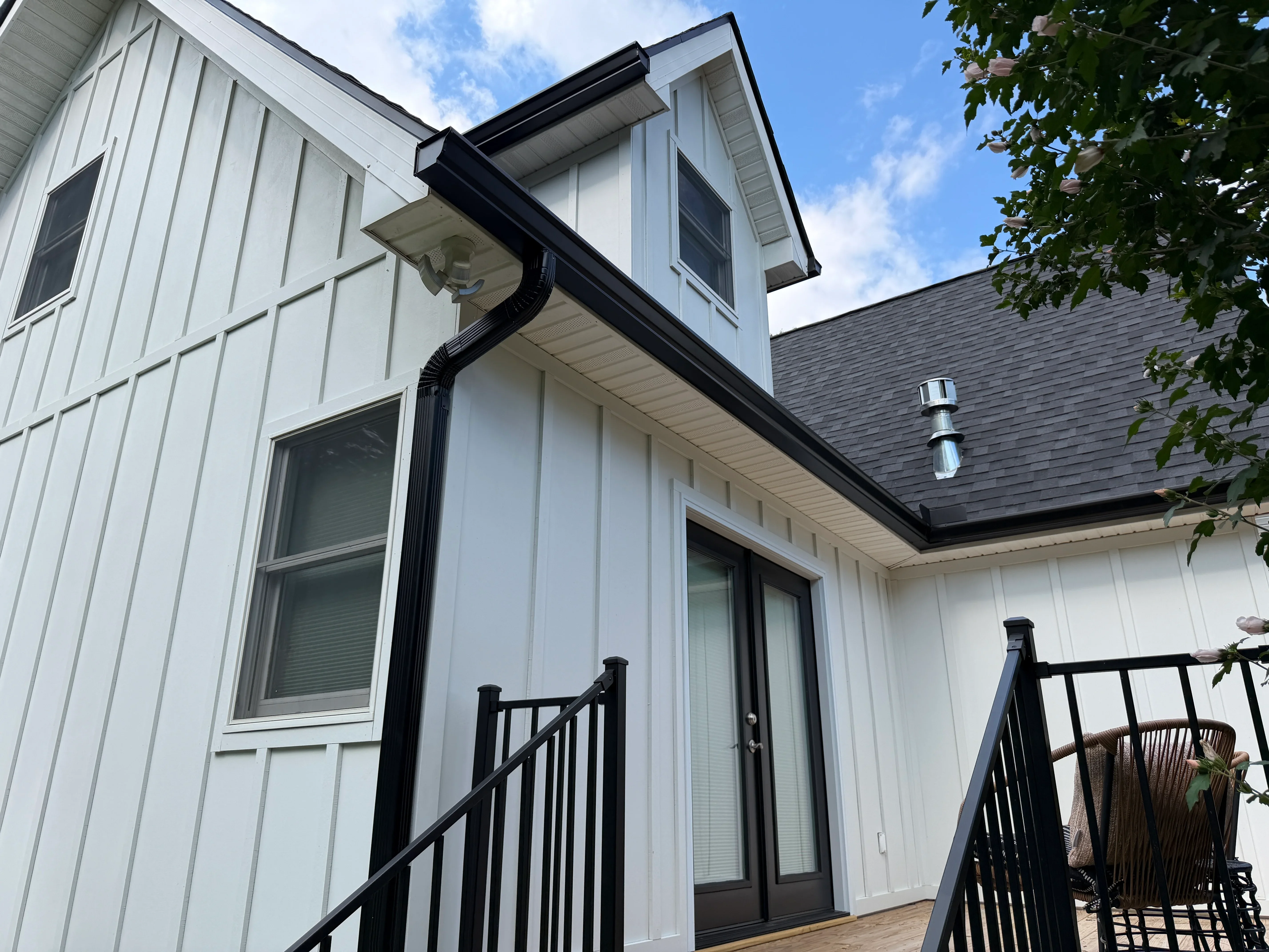 Black seamless gutters and downspout installed on white sided house with black roof