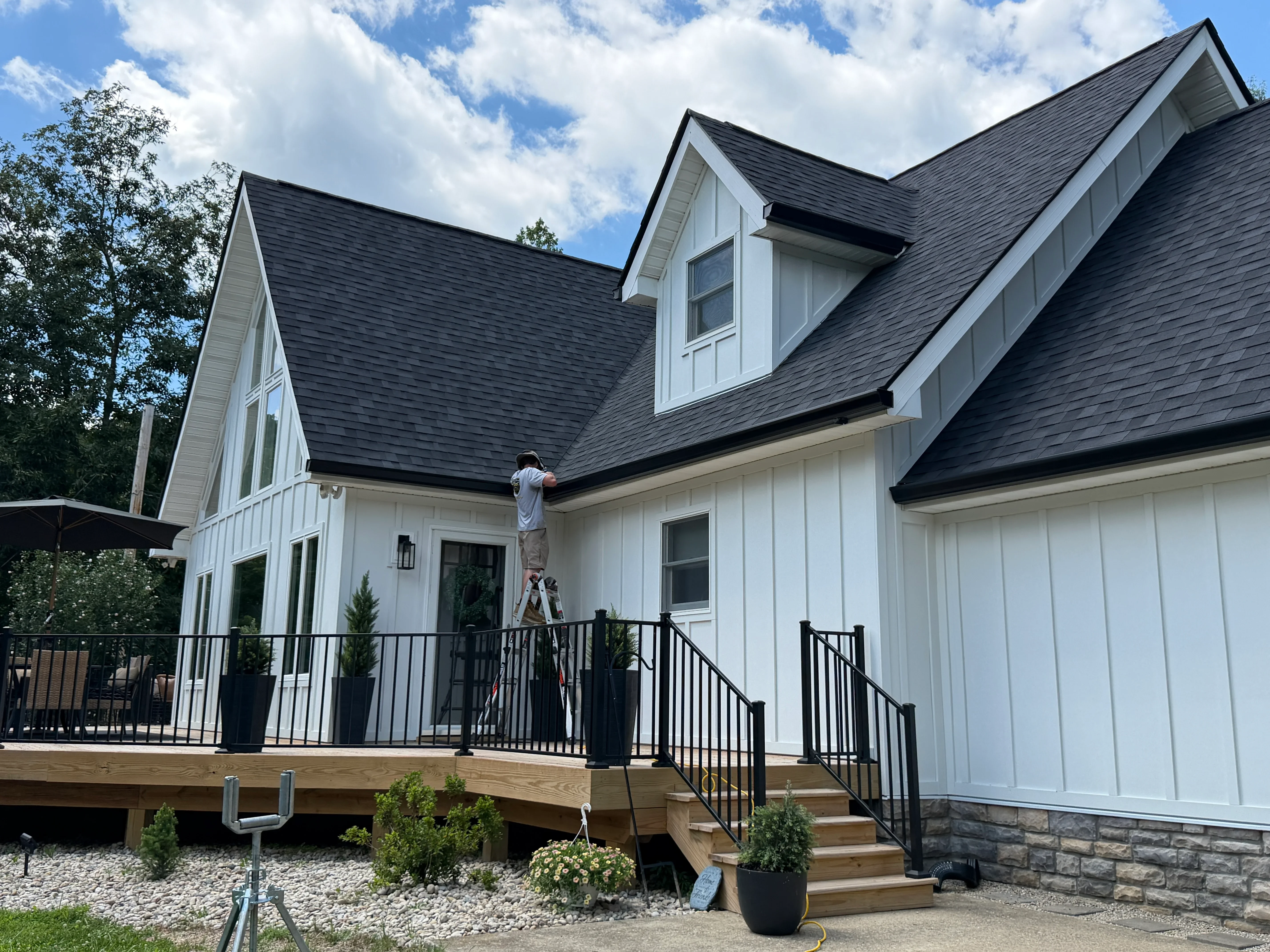 White farmhouse with dark shingle roof, seamless gutters, black metal gutter guards, and wood deck with black railings